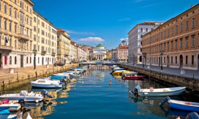 Vista del canale di Trieste in una giornata di bel tempo con il cielo azzurro e due file di barche ormeggiate ai lati.