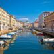 Vista del canale di Trieste in una giornata di bel tempo con il cielo azzurro e due file di barche ormeggiate ai lati.