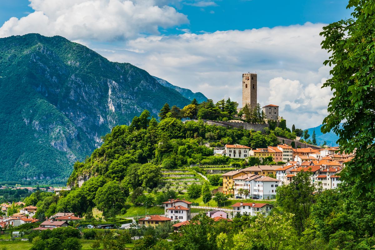 Un panorama del Friuli, in cui si vede un borgo sulle pendici di una collina boscosa sormontata da una torre antica