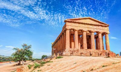 Tempio greco nella Valle dei Templi ad Agrigento con erba bruciata dal sole alla base, una pianta al lato del tempio in una giornata di sole