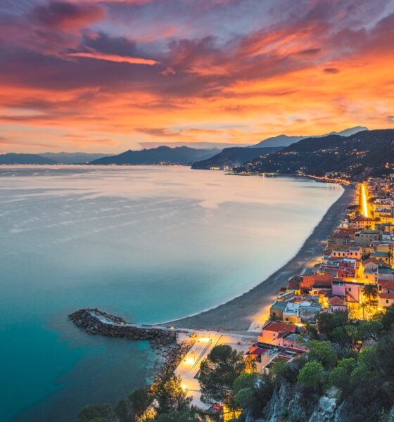 Mare di fronte alla spiaggia di Varigotti con le case illuminate dai lampioni al tramonto con sullo sfondo la cosa della Riviera di Ponente della Liguria