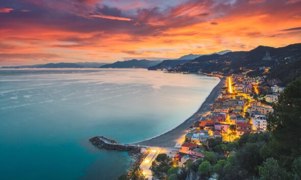Mare di fronte alla spiaggia di Varigotti con le case illuminate dai lampioni al tramonto con sullo sfondo la cosa della Riviera di Ponente della Liguria
