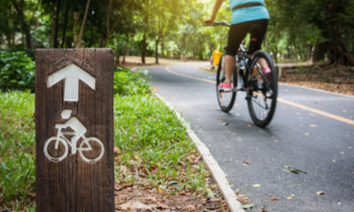 Segnale di legno in primo piano con una donna in bicicletta su una ciclabile asfaltata nel parco