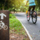 Segnale di legno in primo piano con una donna in bicicletta su una ciclabile asfaltata nel parco