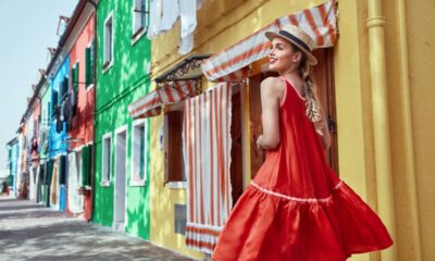 Ragazza vestita di rosso cammina lungo una via di case dai colori accesi a Burano, Venezia