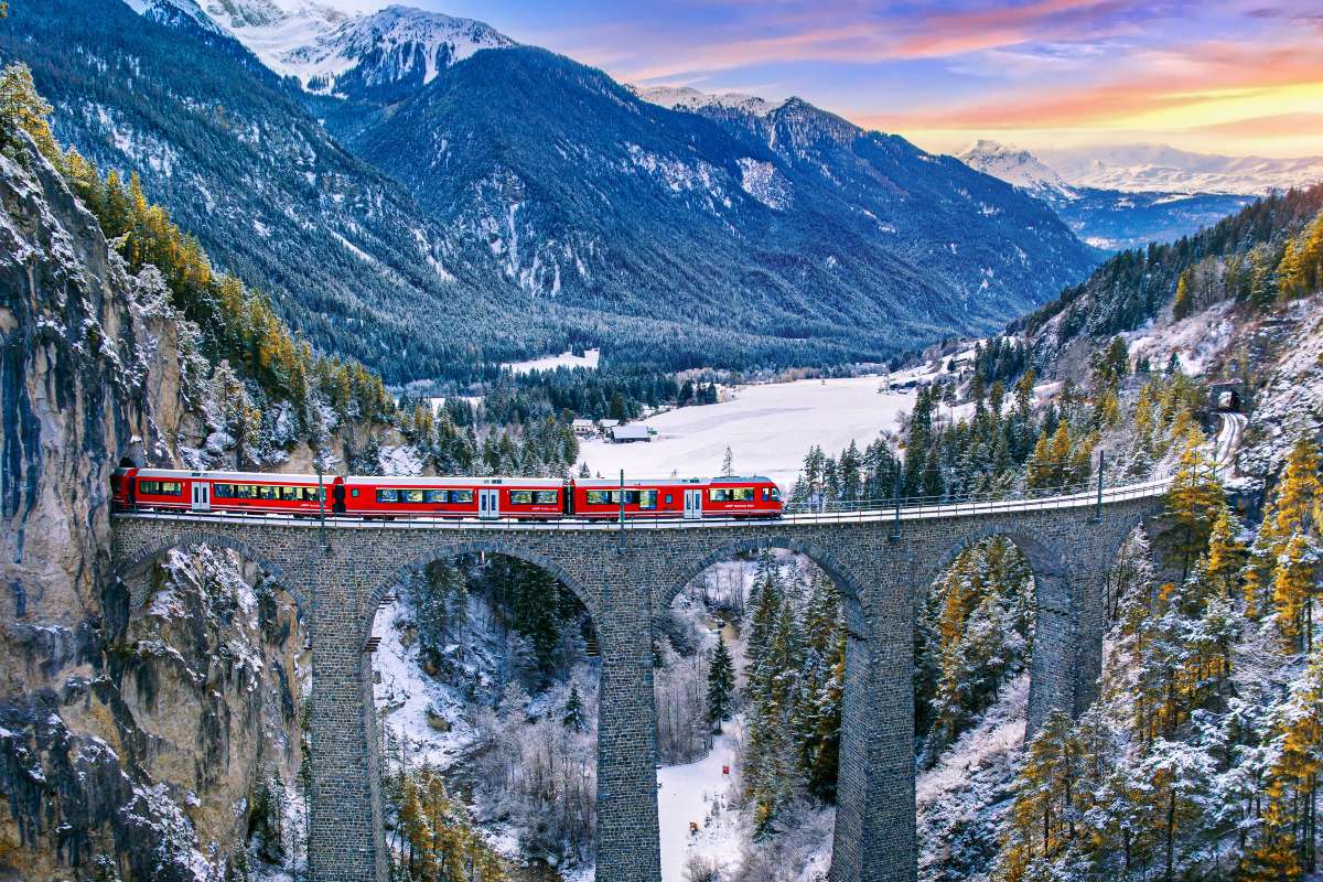 Treno che transita sul ponte Filisur in Svizzera con sullo sfondo le montagne alpine