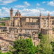 Centro storico di Urbino con delle piante in primo piano e sullo sfondo delle colline in una giornata di sole
