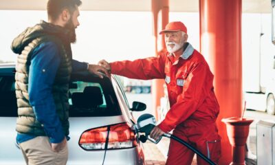 Benzinaio sorridente con tuta rossa che fa il pieno di carburante all'auto di una persona