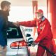Benzinaio sorridente con tuta rossa che fa il pieno di carburante all'auto di una persona