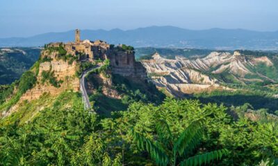 Città vecchia di Civita di Bagnoreggio in cima alla montagna con il suo ponte che porta al borgo, della vegetazione in primo piano e sullo sfondo altri monti del Lazio