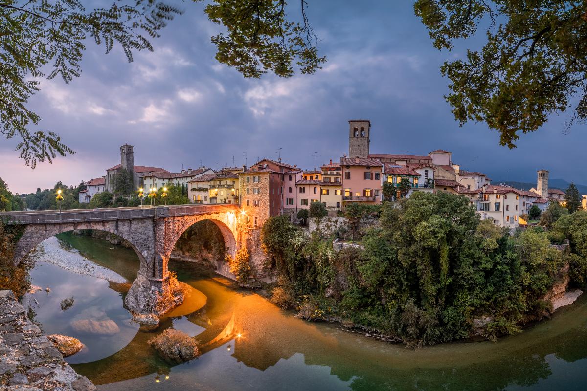 Vista di Cividale del Friuli all'imbrunire con in primo piano il fiume Natisone e il Ponte del Diavolo illuminato