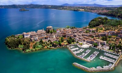 Porticciolo del Lago di Bolsena con le case del centro storico e le barche ormeggiate, con sullo sfondo il lago e la sua sponda con una piccola isola