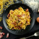 Un piatto scuro riempito di spaghetti alla Carbonara e a fianco un uovo, il guanciale a tocchetti e il pecorino