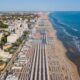Spiaggia della Romagna con stabilimenti e file di ombrelloni con da un lato il mare e dall'altro le case del centro abitato in una giornata limpida
