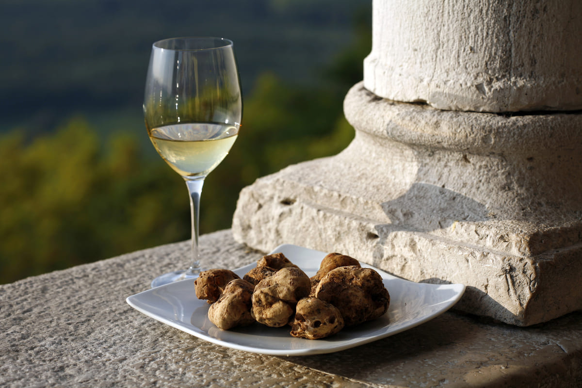 Un piatto di tartufi bianchi ed un calice di vino vicino al basamento di una colonna