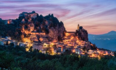 Borgo di Bagnoli del Trigno con le case illuminate di sera con in primo piano delle fronde degli alberi e sullo sfondo la vallata