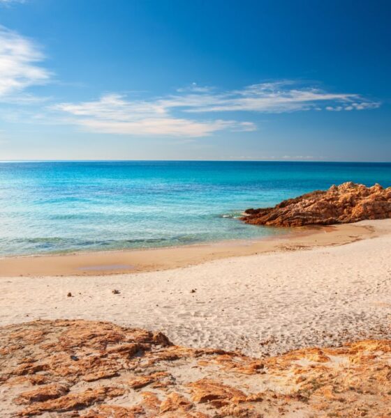 Spiaggia di Santa Margherita di Pula con sabbia e delle rocce che finiscono a filo acqua del mare