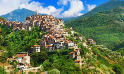 Case sulla parete di una montagna con tanta vegetazione che le circondano con sullo sfondo altre montagne ricoperte di vegetazione