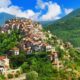 Case sulla parete di una montagna con tanta vegetazione che le circondano con sullo sfondo altre montagne ricoperte di vegetazione
