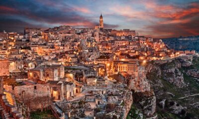 Case antiche del centro storico di Matera con le sue rocce e il campanile sulla cima, illuminate dalle luci al calar della sera