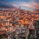 Case antiche del centro storico di Matera con le sue rocce e il campanile sulla cima, illuminate dalle luci al calar della sera
