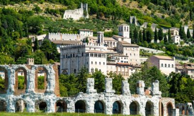 Edifici storici di Gubbio che si sviluppano sulla parete con vegetazione di una montagna con in primo piano le rovine dell'anfiteatro romano