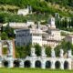 Edifici storici di Gubbio che si sviluppano sulla parete con vegetazione di una montagna con in primo piano le rovine dell'anfiteatro romano