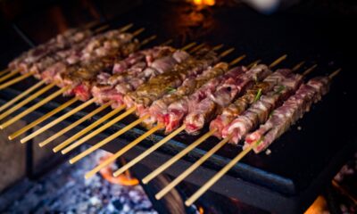 Una fila di arrosticini sulla piastra mentre cuociono con degli aghi di rosmarino