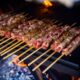 Una fila di arrosticini sulla piastra mentre cuociono con degli aghi di rosmarino