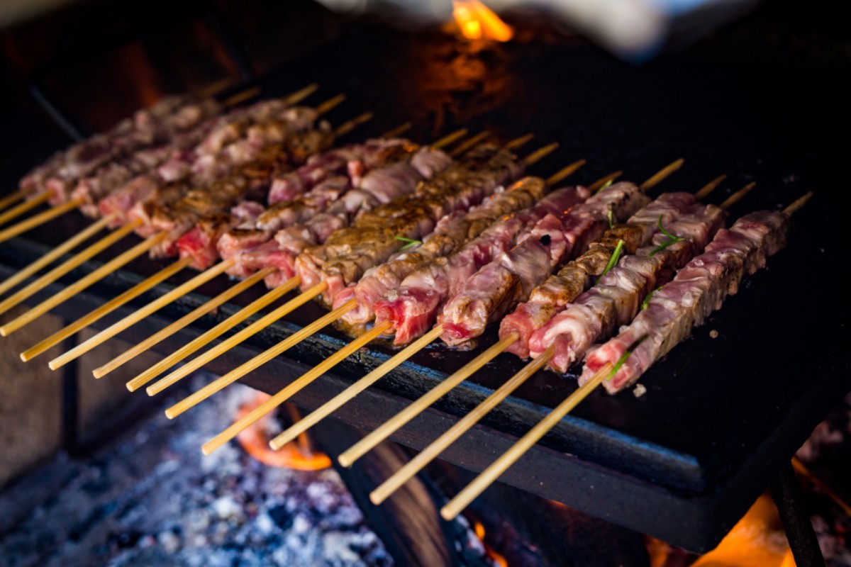 Una fila di arrosticini sulla piastra mentre cuociono con degli aghi di rosmarino