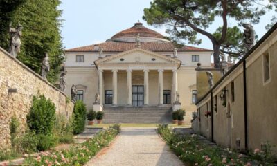 Facciata di Villa Capra con le sue colonne e in primo piano una stradina sterrata con delle aiuole ai lati e le mura del giardino della villa ai lati