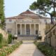 Facciata di Villa Capra con le sue colonne e in primo piano una stradina sterrata con delle aiuole ai lati e le mura del giardino della villa ai lati